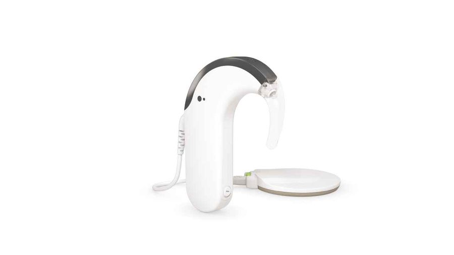 Ein schlankes, weißes Cochlea-Implantat mit einem durchscheinenden Ohrhaken und einem angeschlossenen runden Sender liegt auf einem weißen Hintergrund.