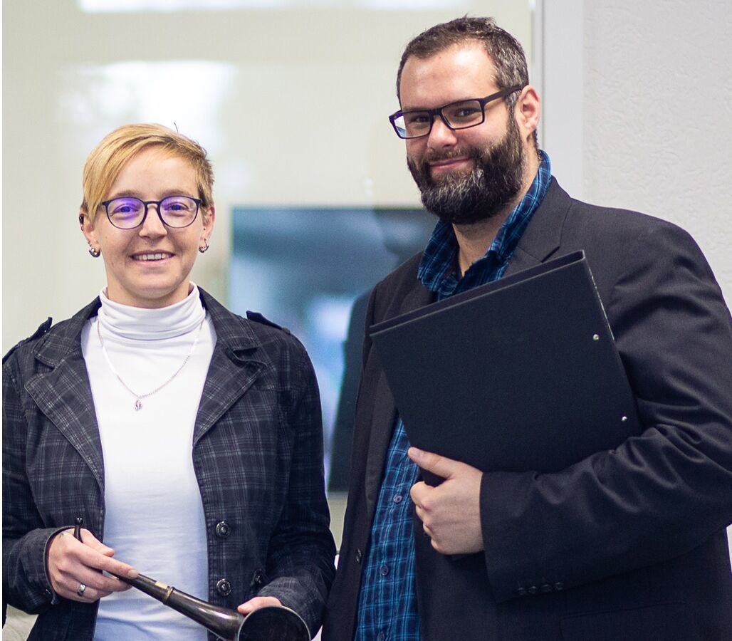 Zwei Fachpersonen präsentieren ein historisches Hörinstrument in einem audiologischen Umfeld.